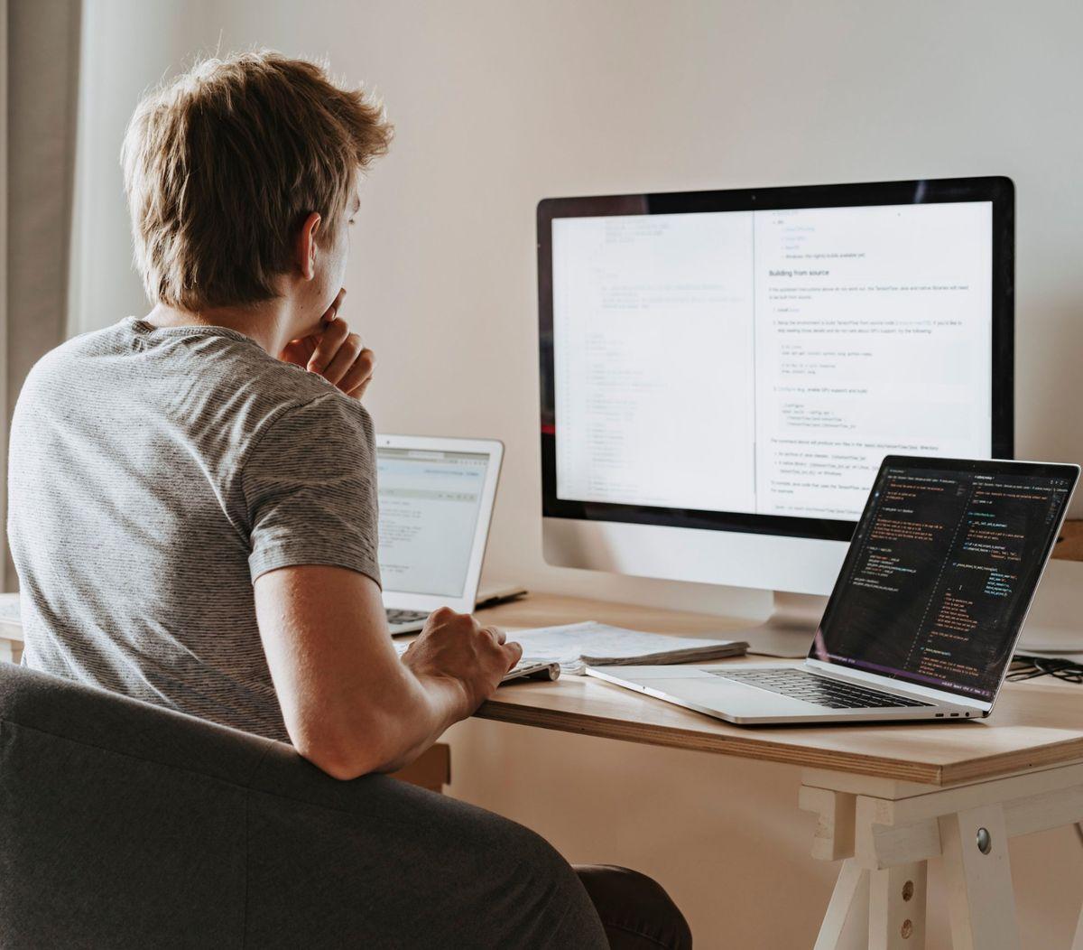 Developer reviewing code across a laptop and desktop monitor